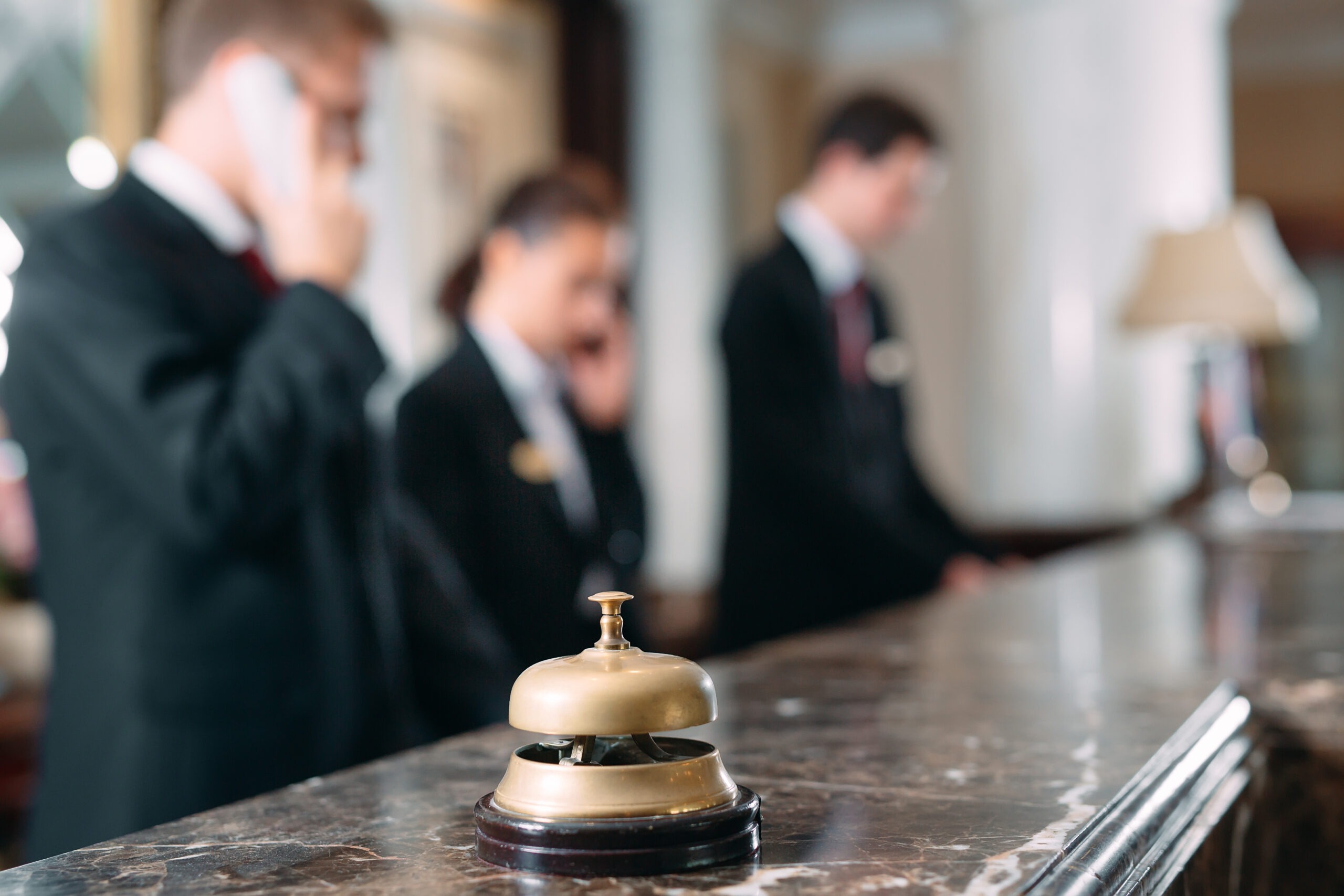 Photo of 3 concierges working at the desk with a reception bell in the foreground