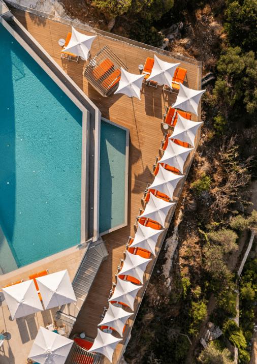 Aerial view of a luxury poolside area with white sun umbrellas and orange lounge chairs